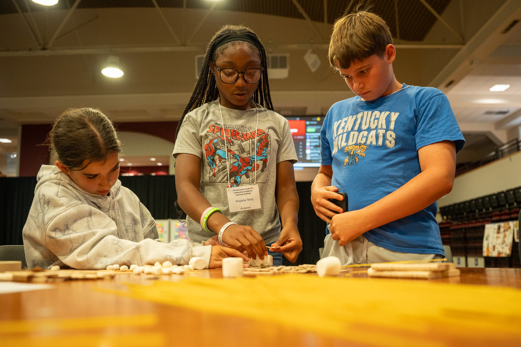 Three students examine pasta and marshmallows as they attempt to build a tower