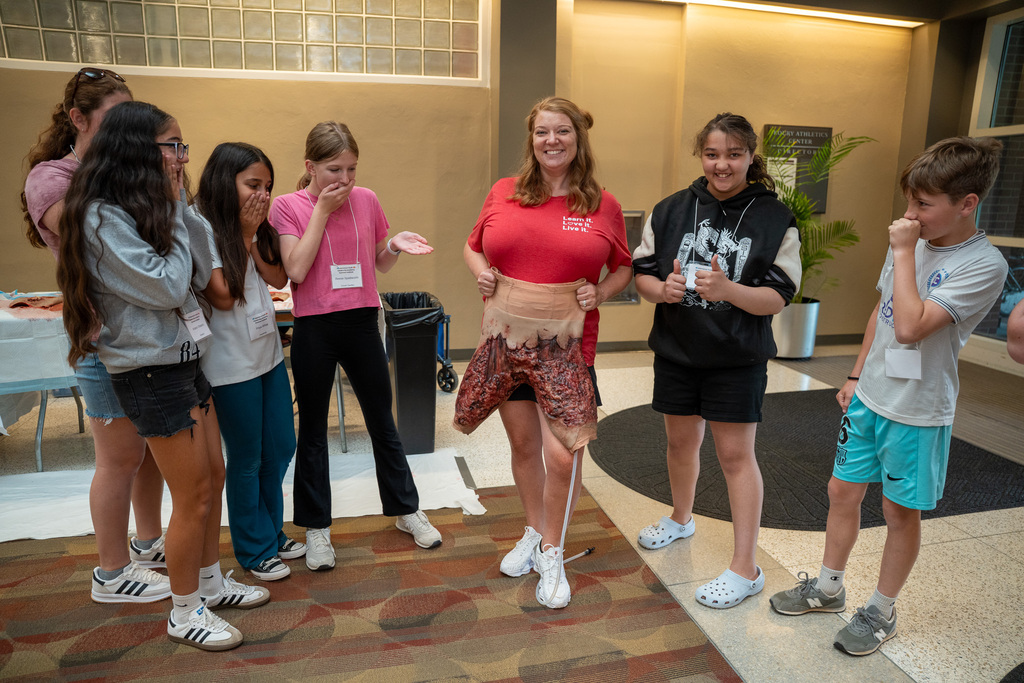 A CTE staff member in a red shirt holds up a latex burn thigh prop next to "surprised" students