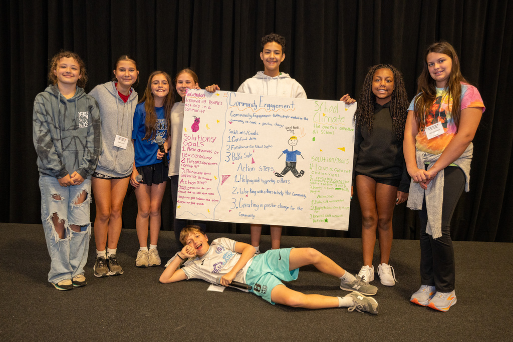 A group of middle school students gathered behind their poster for a group project
