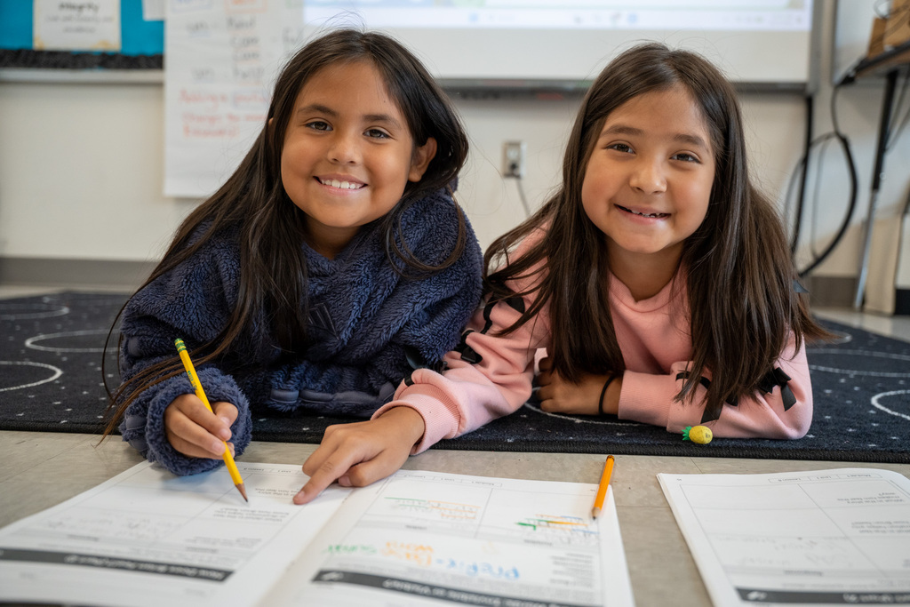 Two students look up and smile while working on a reading assignment