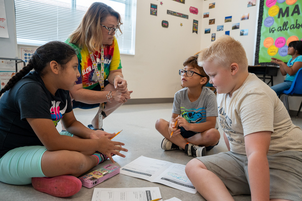 A teacher in a tye-dye school shirt checks in on a small group of students