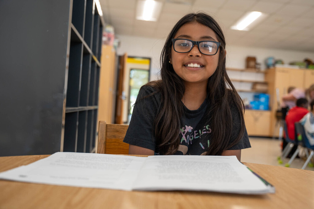 A girl in a black t-shirt looks up and smiles with a reading passage in front of her