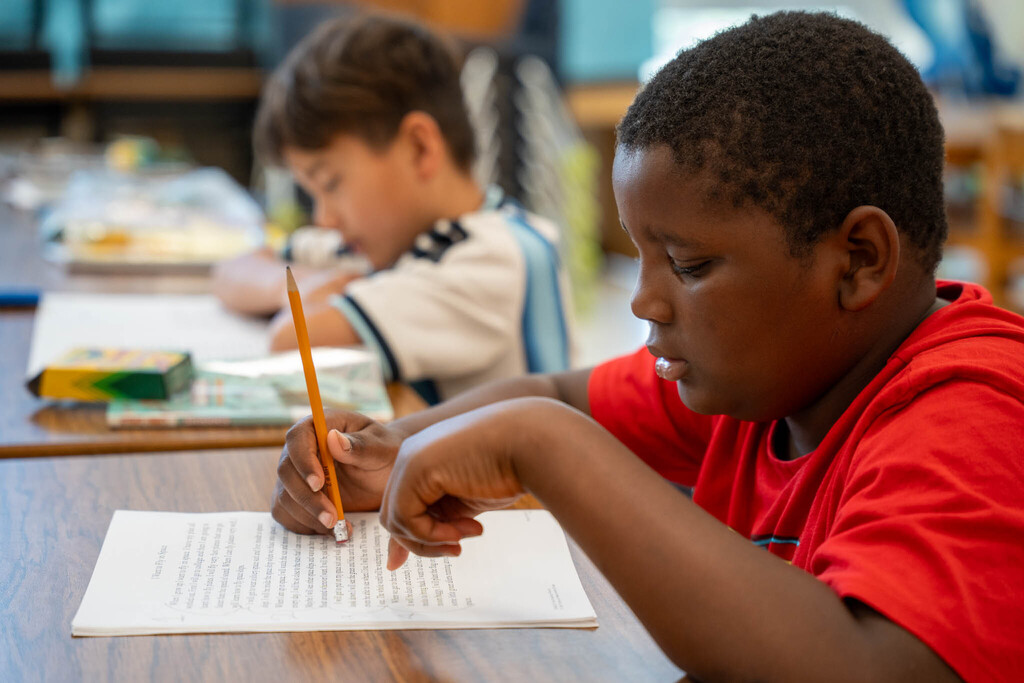 Two elementary students concentrate on reading passages, one holding a pencil as he reads it carefully