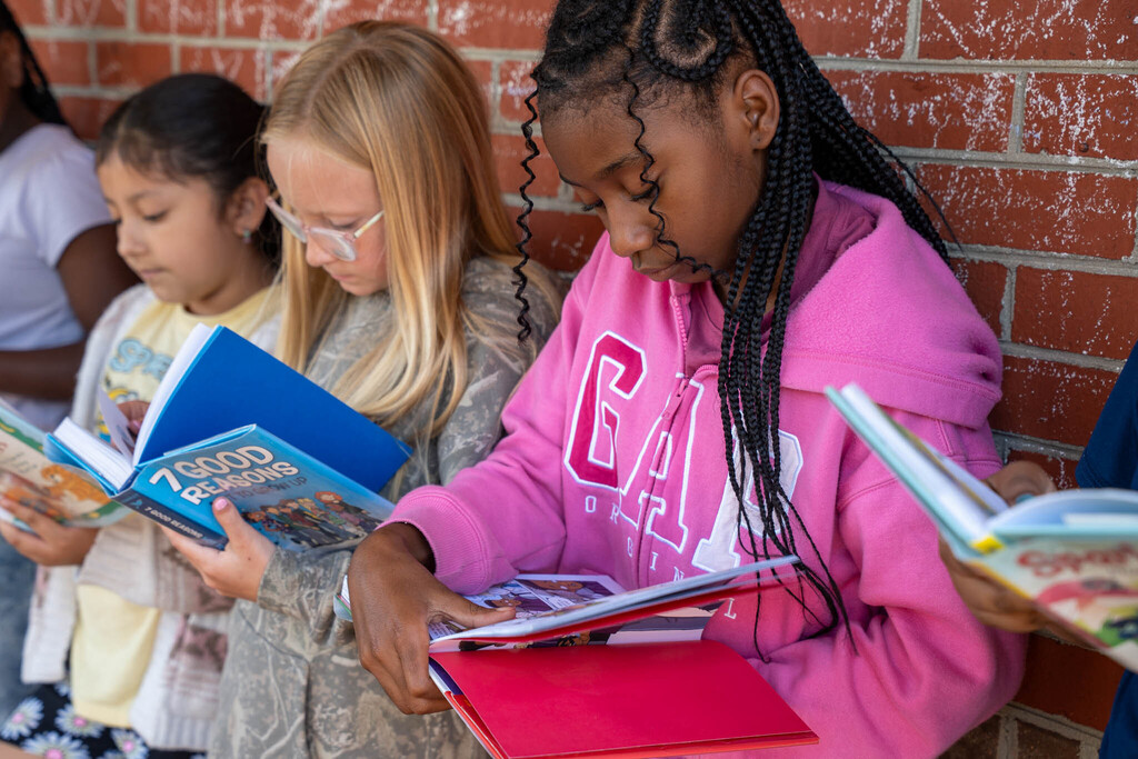 A group of elementary students read books against a brick wall