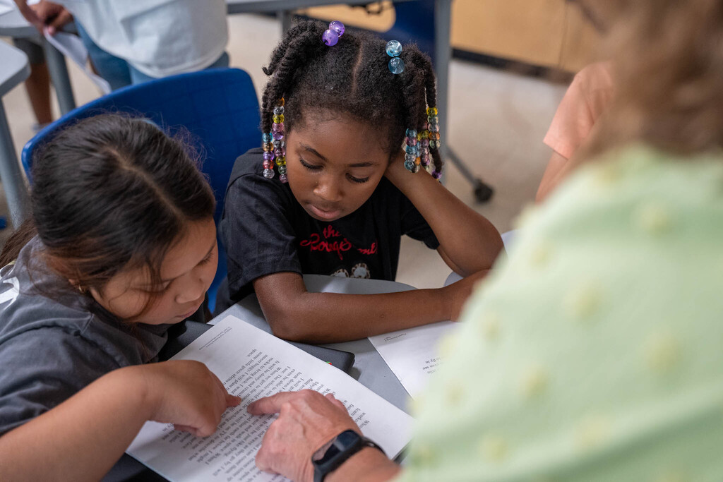 Two elementary students respond to a reading passage indicated by a teacher pointing