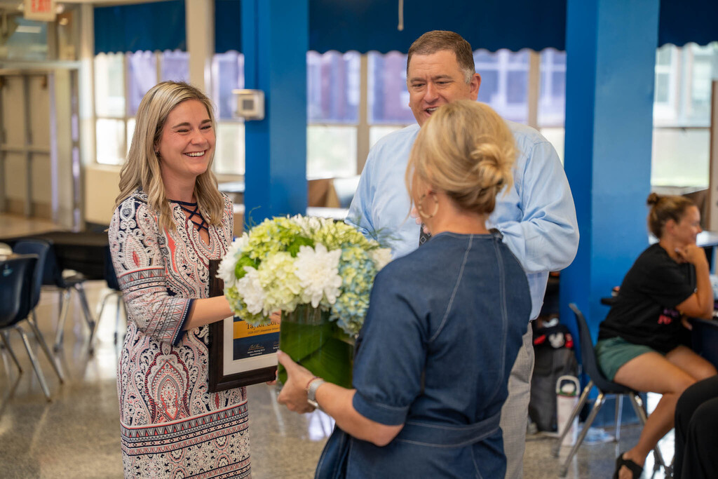 Taylor Corcoran smiles as she receives a bouquet of flowers and a framed award during a staff meeting recognition.
