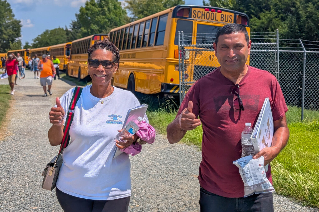 Two bus drivers give thumbs up as they make their way to their school buses