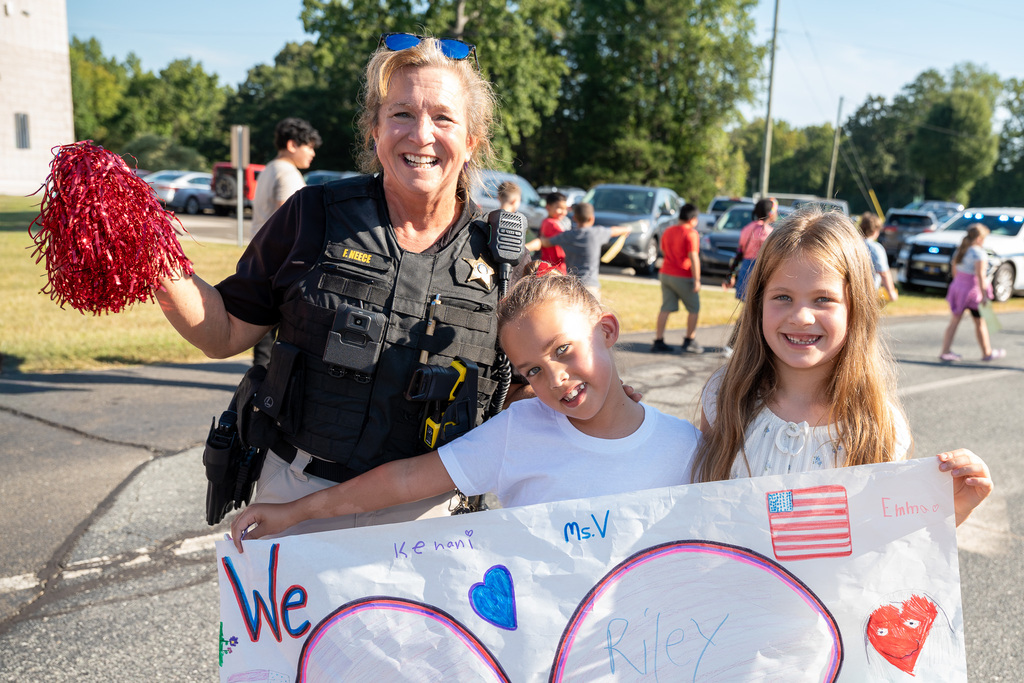 A school resource officer stands next to two young girls behind a We Love First Responders poster.