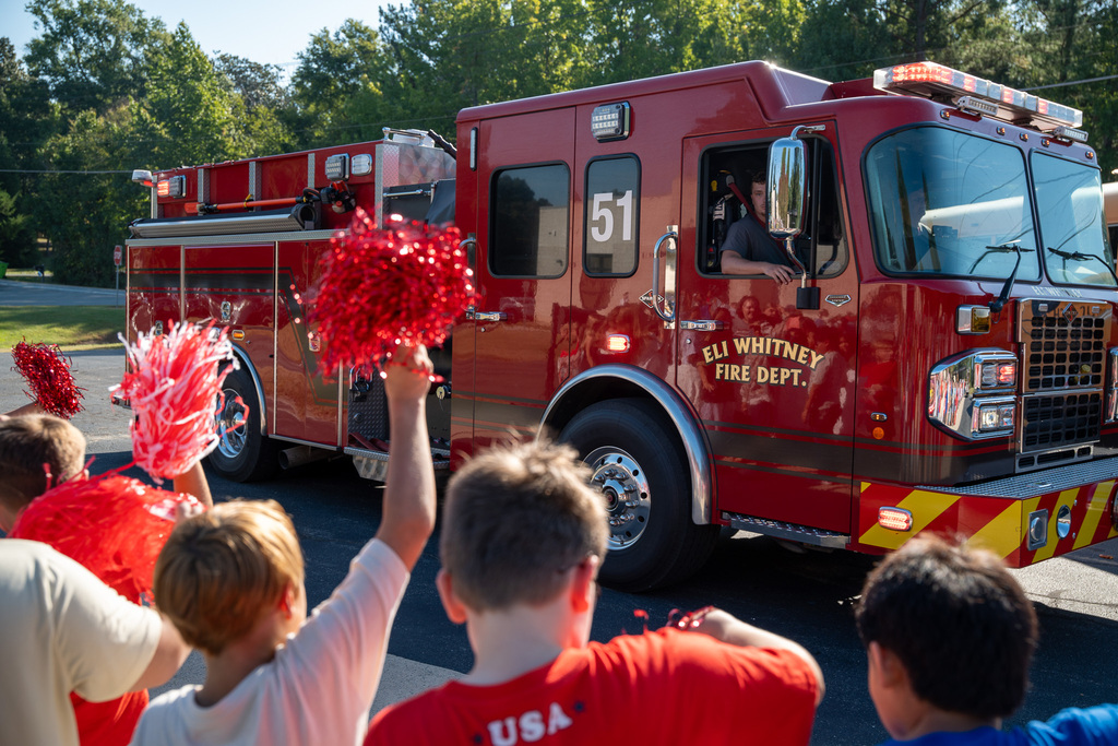 Elementary students watch and wave red pompoms as an Eli Whitney fire truck drives by.