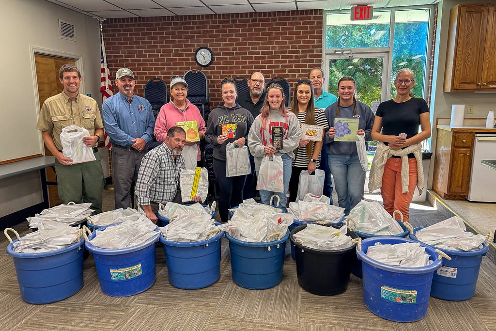 Agri-Business Commitee members stand behind many large bins full of bags of items for elementary students