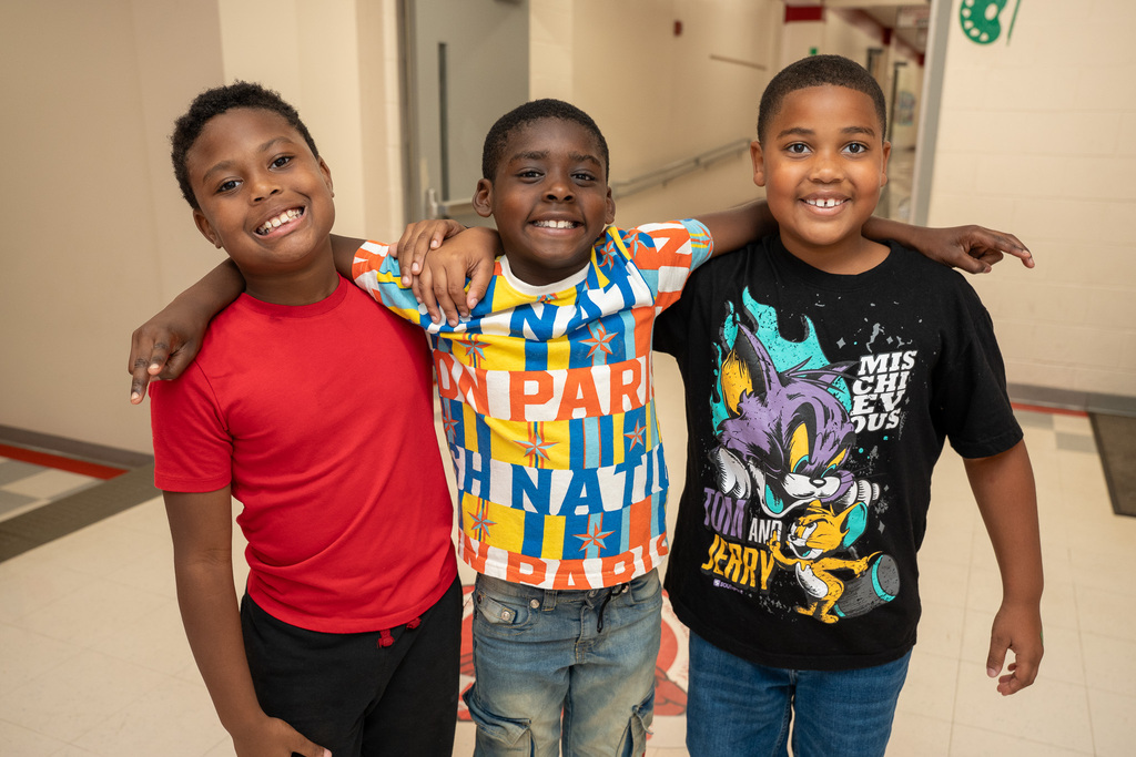 Three elementary boys stand beside each other with their arms over each other's shouldewrs