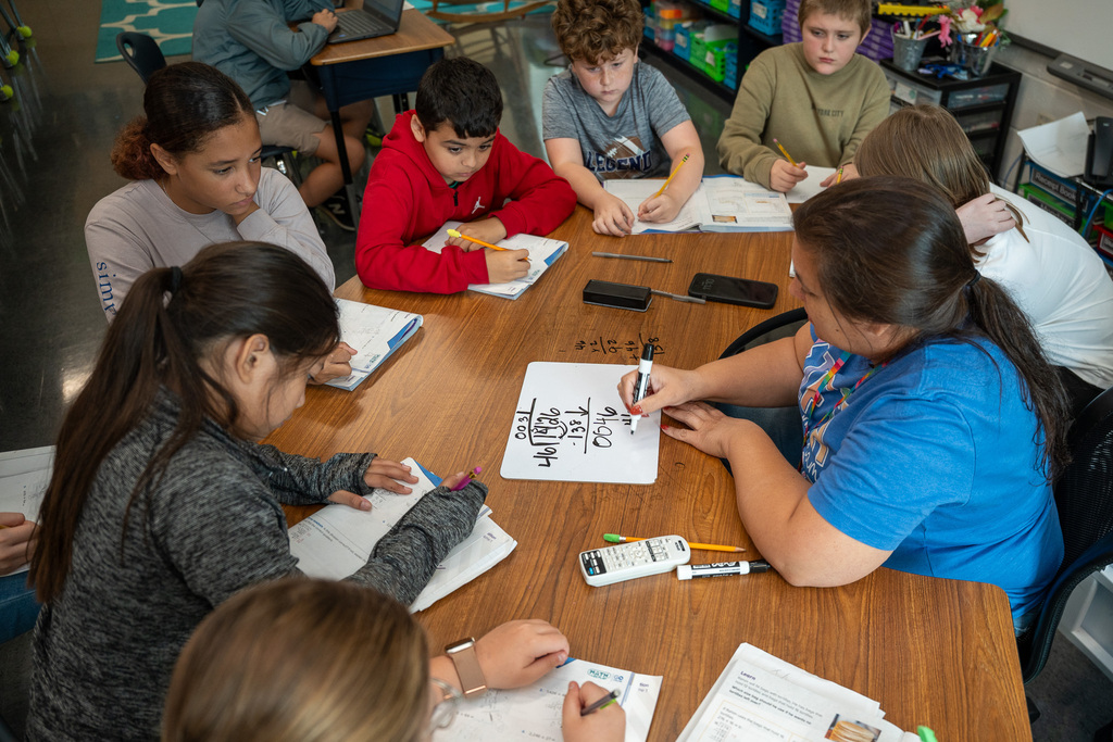 A teacher models a math equation as students in a small group setting observe carefully