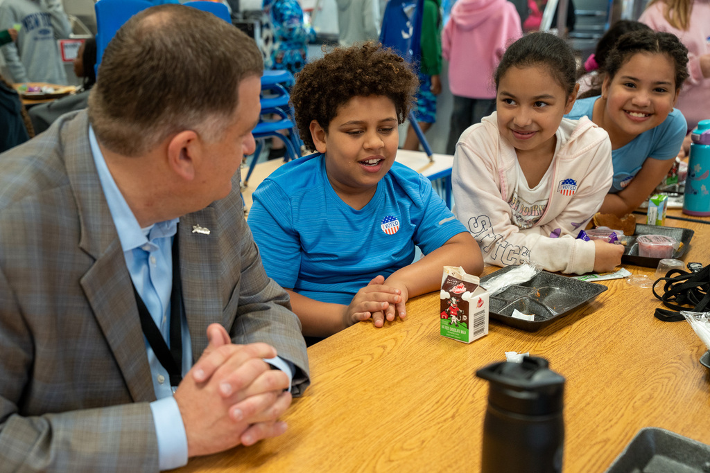 Superintendent Dr. Fleming talks with students at a lunch table.