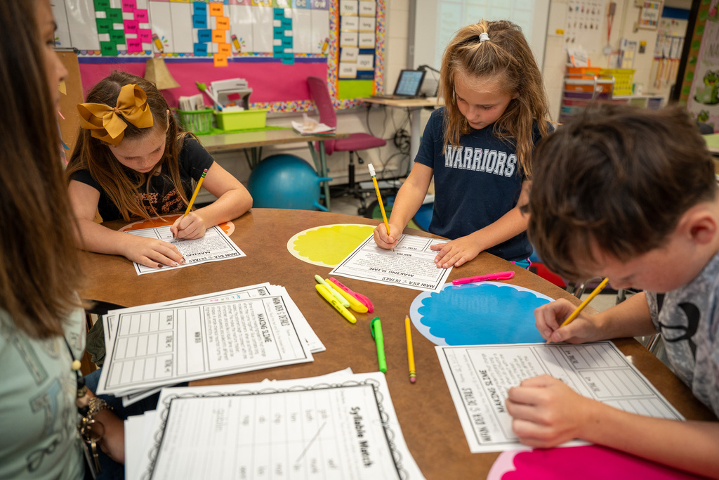A teacher provides guidance as a small group of elementary students write during a guided lesson.