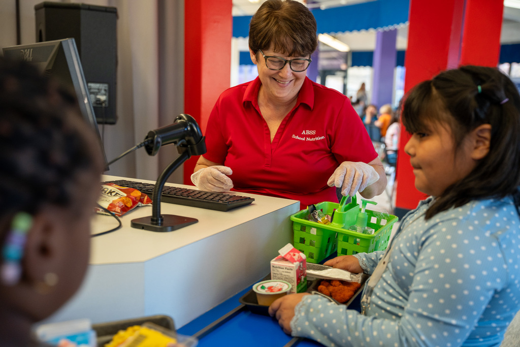 A school nutrition staff wearing a red shirt processes student orders in a lunch line