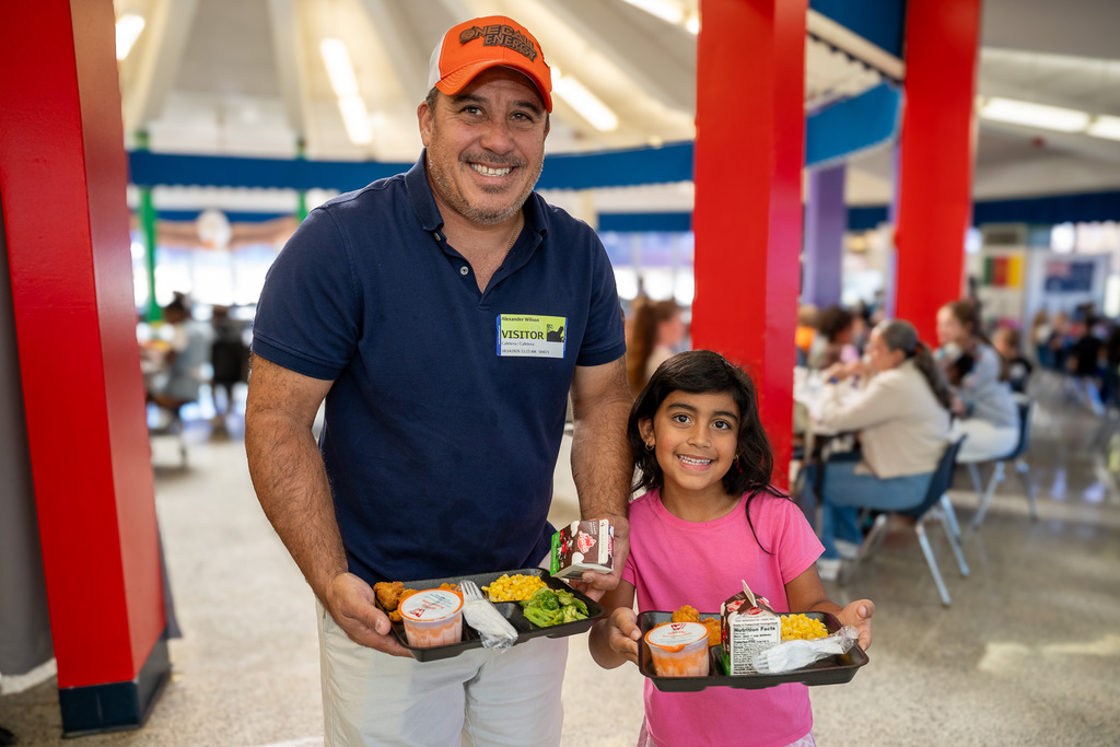 A father and his daughter hold school lunch trays in the cafeteria 