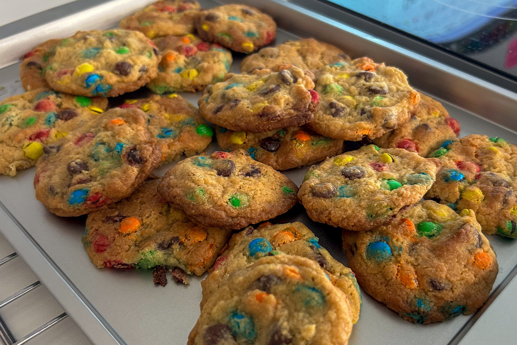 A baking tray of freshly baked chocolate chip cookies with colorful candy pieces.