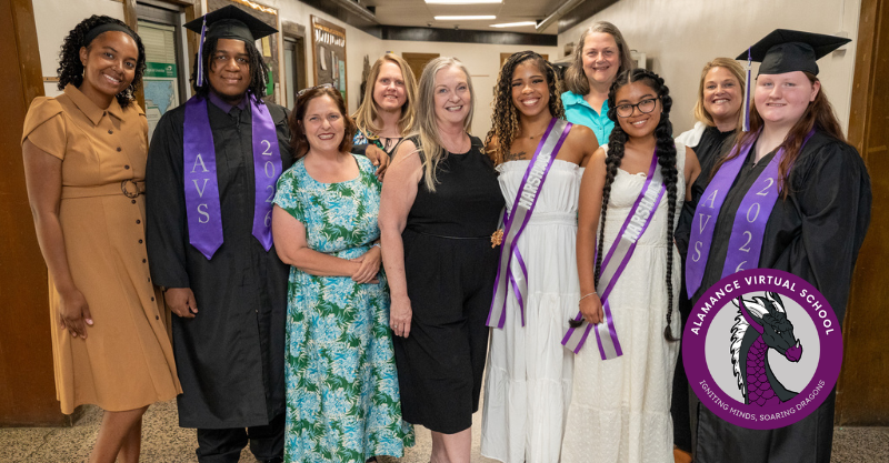 Group of staff and high school graduates, who are wearing black and purple attire, in a high school hallway