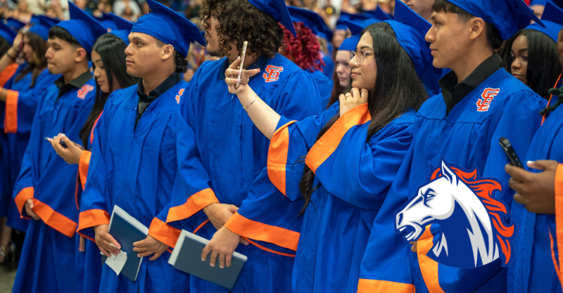 Southeast Alamance High School graduates in the front of row of the graduation ceremony, standing, looking towards the stage.  A female student is taking a selfie.