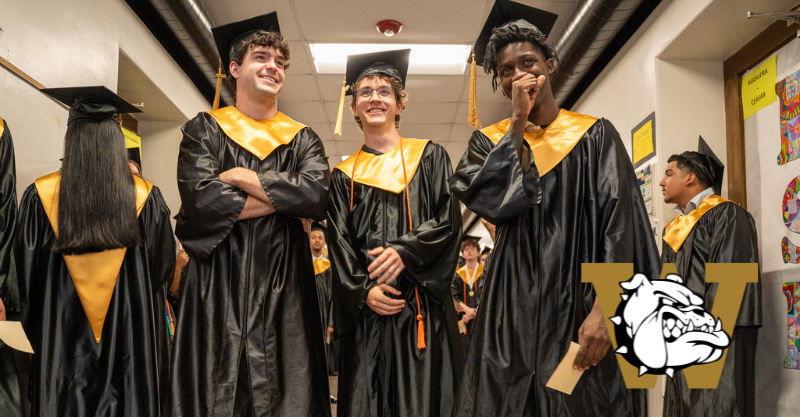 High school seniors wearing black and yellow graduation attire prior to their graduation ceremony.  Three male students are standing beside each other in the middle of the hallway, captured with a low camera angle.