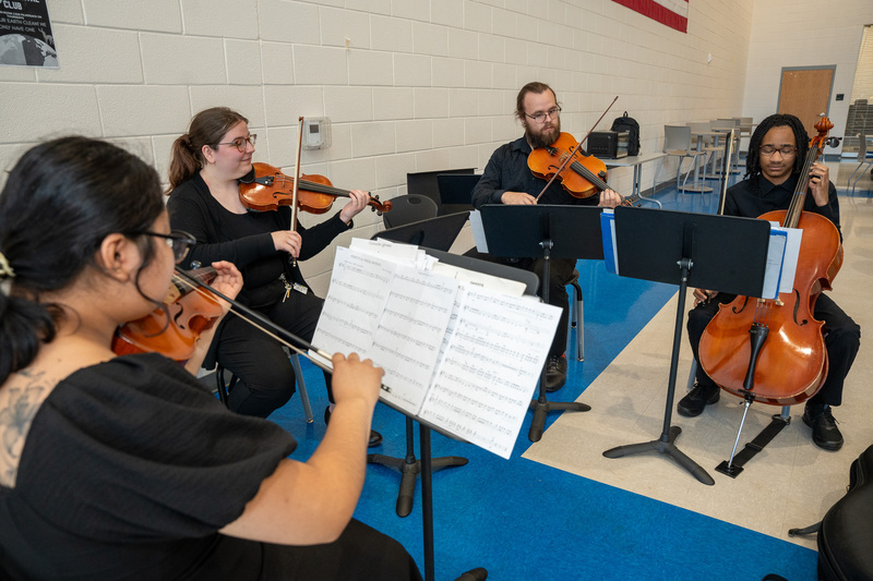 A group of four Cummings orchestra ensemble members playing string instruments in a large cafeteria