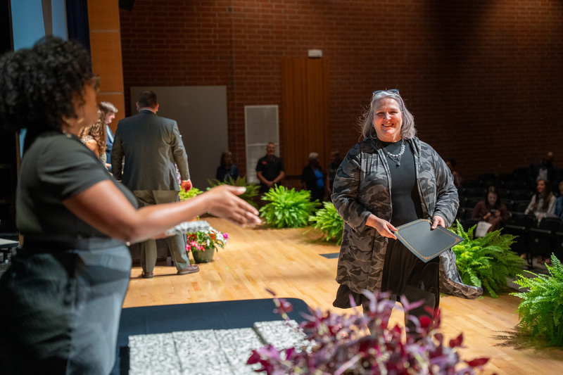 A retiree walks towards a Human Resources staff member to accept a certificate