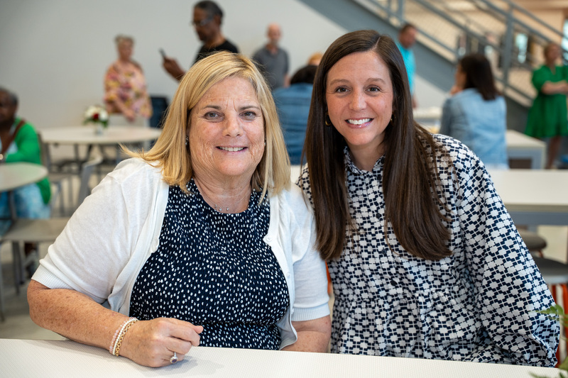 A retiree wearing a blue polka dot shirt and white sweater smiles next to a principal wearing a blue patterned shirt