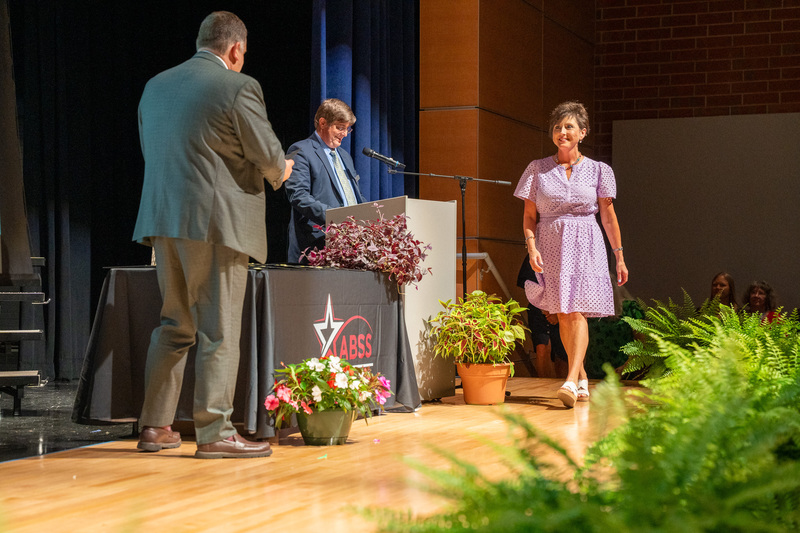 A retiree walks up to accept a certificate from the superintendent on stage at the retirement celenbration