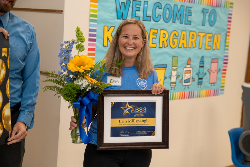 Principal Erin Millspaugh holding a ABSS Principal of the Year plaque and flower bouquet