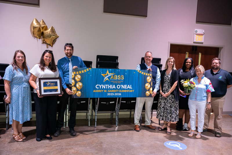 Cynthia O'Neal stands with district staff holding a recognition banner, balloons, and a plaque recognizing her as Assistant Principal of the Year