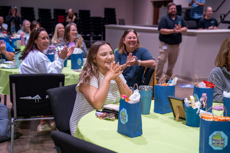 Staff look happily towards Cynthia O'Neal as she is recognized at a staff meeting