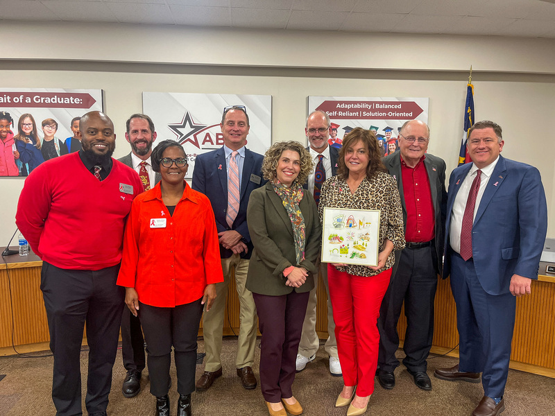 Tracey Grazer from Impact Alamance standing with the Board and an artwork commemorating the partnership between ABSS and Impact Alamance