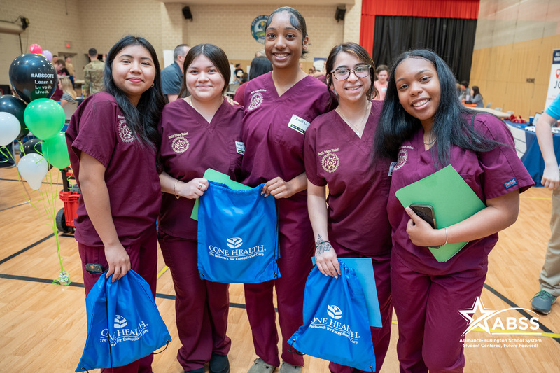 Five students wearing nurse scrubs and holding career bags at a senior job fair