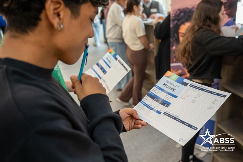 A student holding his pencil to his face while closely examining a Reality of Money activity pamphlet