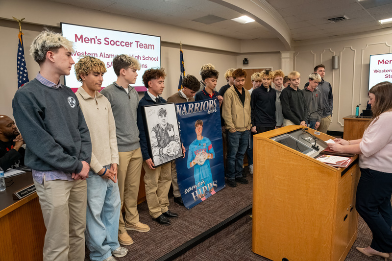 Western boys soccer team at the front of the board room holding portrait of Eamon Hipps