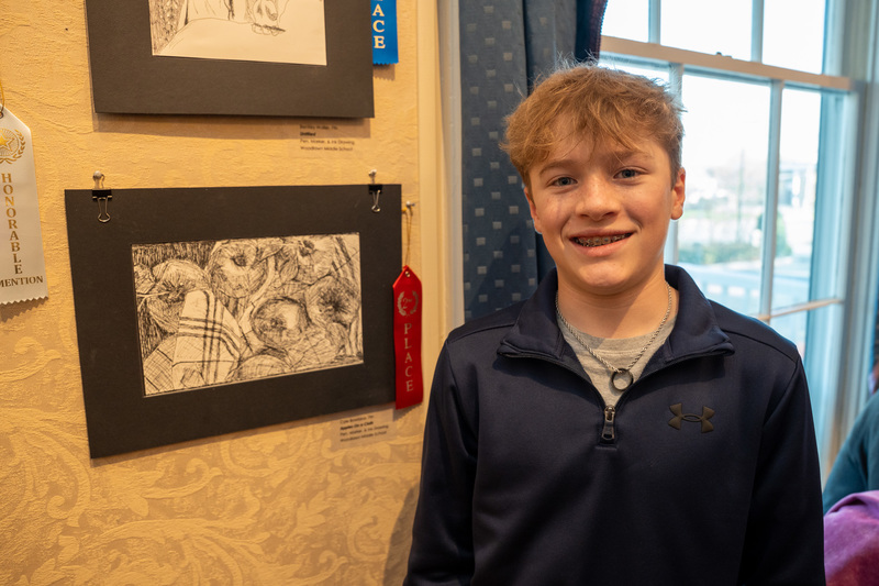 Cole Bowland wearing a blue Under Armour athletic half-zip shirt stands beside his art