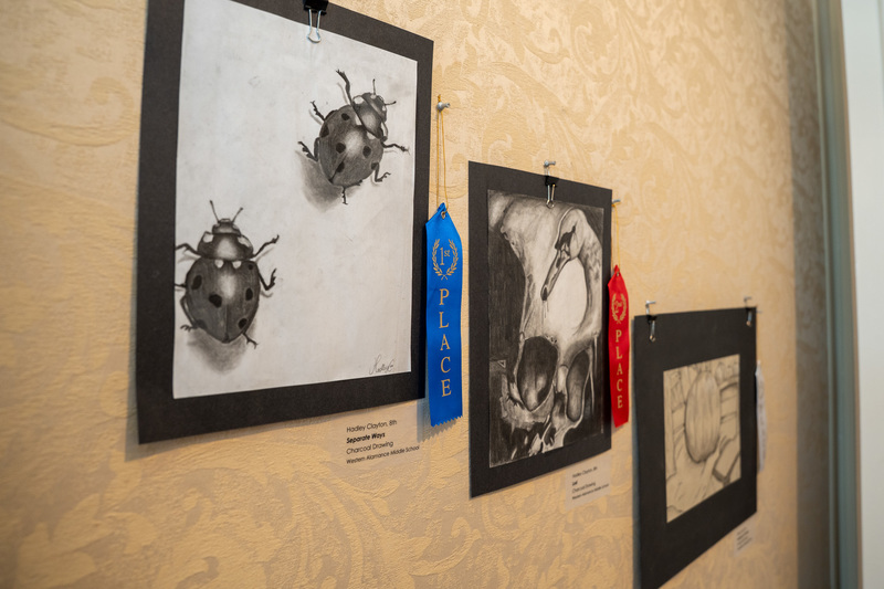 Three charcoal drawings on display with focus primarily on Hadley Clayton's winning piece depicting two ladybugs drawn in charcoal