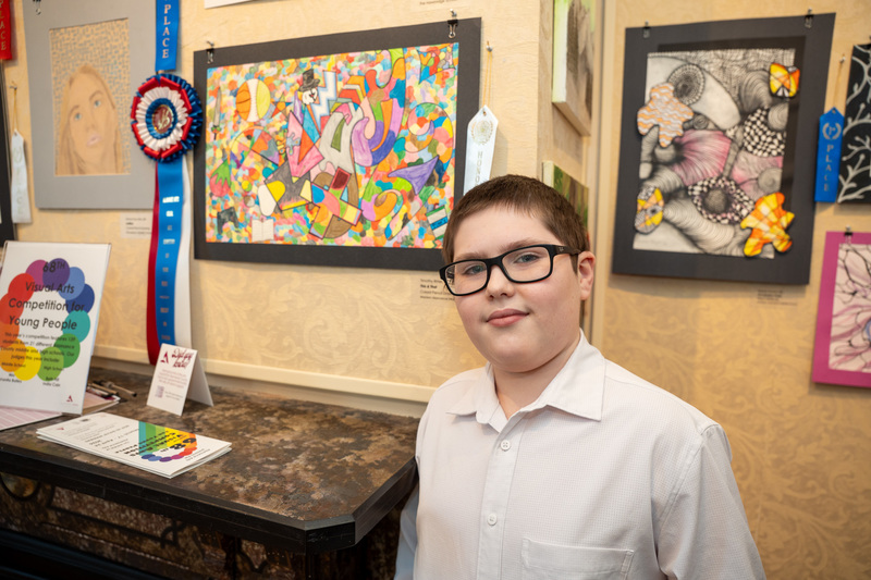 Student Timothy Ritter standing beside his winning piece This or That which is a collage or various elements in colorful color pencil style