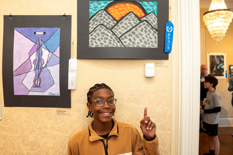 Taylor Lindsey pointing up to his first place tempera painting of a sun over mountains