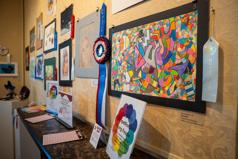 A large display of student artwork, including Best in Show for Middle School, with a sign for the event in the foreground