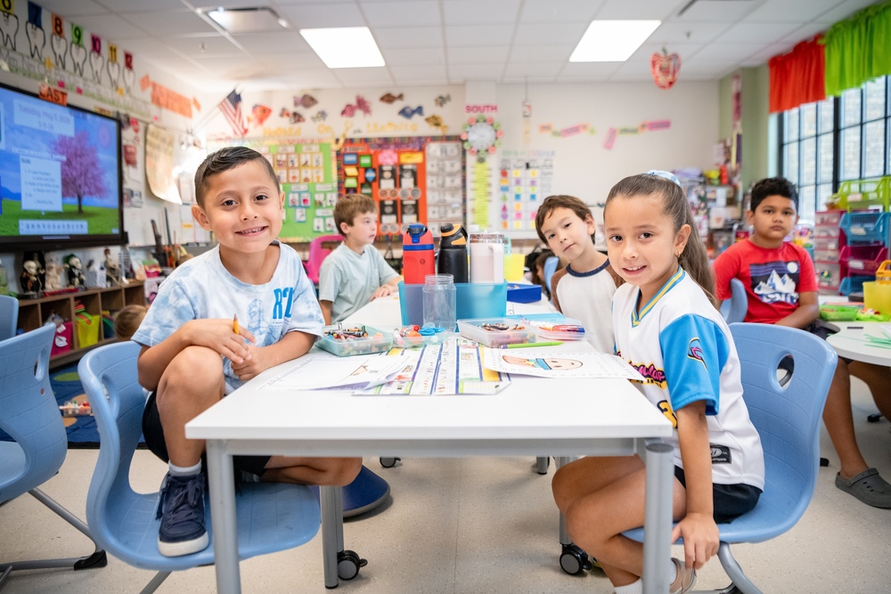 Three students smiling at their desk