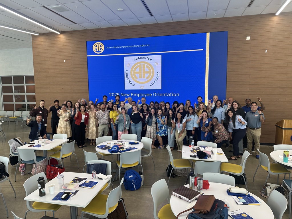 Group of new employees pose for picture in the HS cafeteria in front of screen
