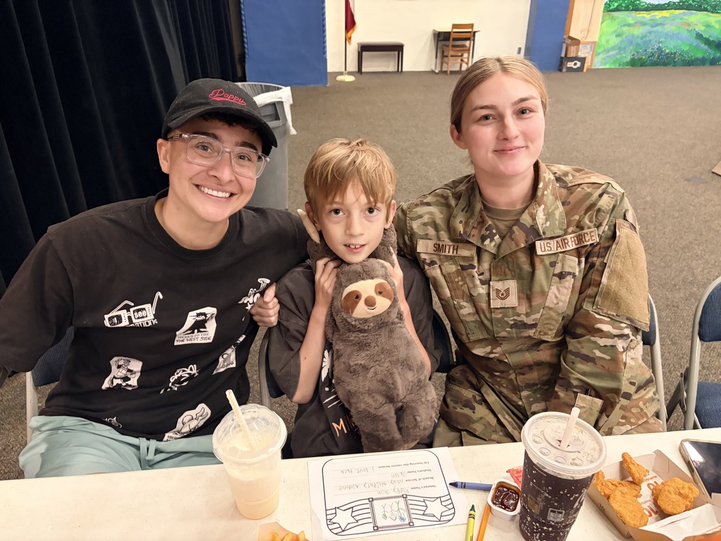 Parents eat lunch with child who is holding sloth stuffed animal