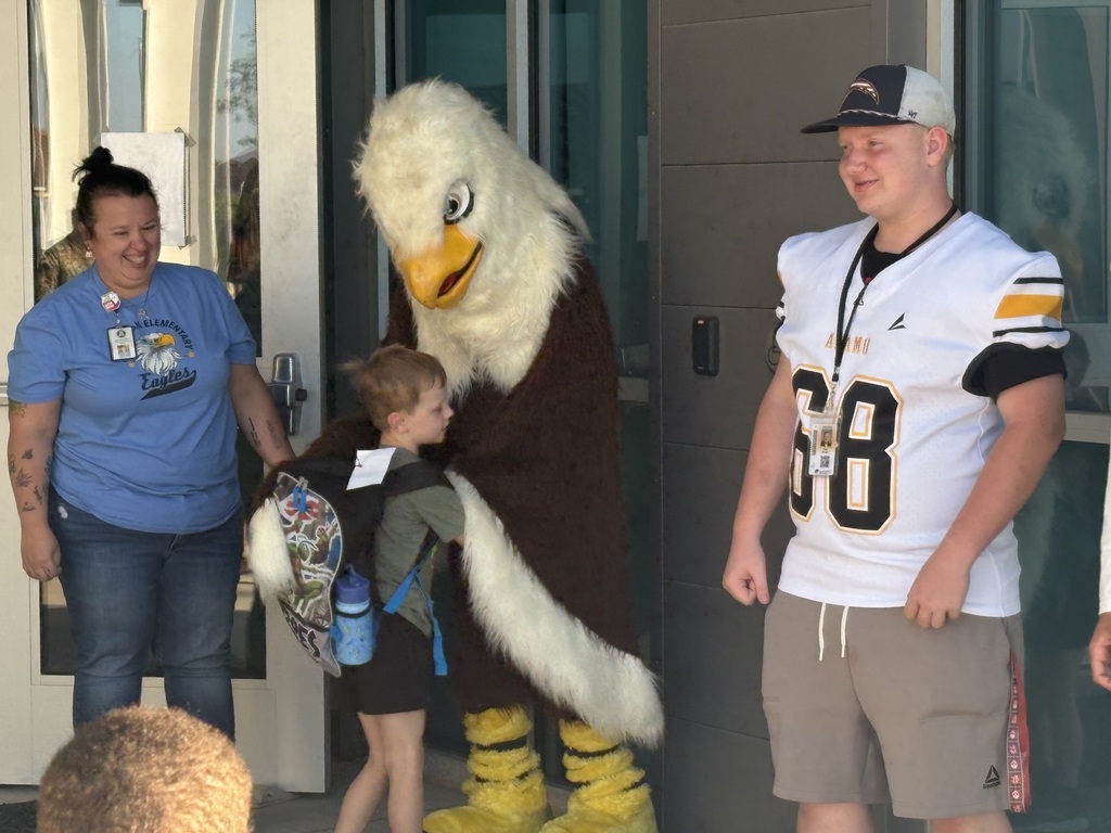 elementary school mascot hugging elementary school student. football player standing by