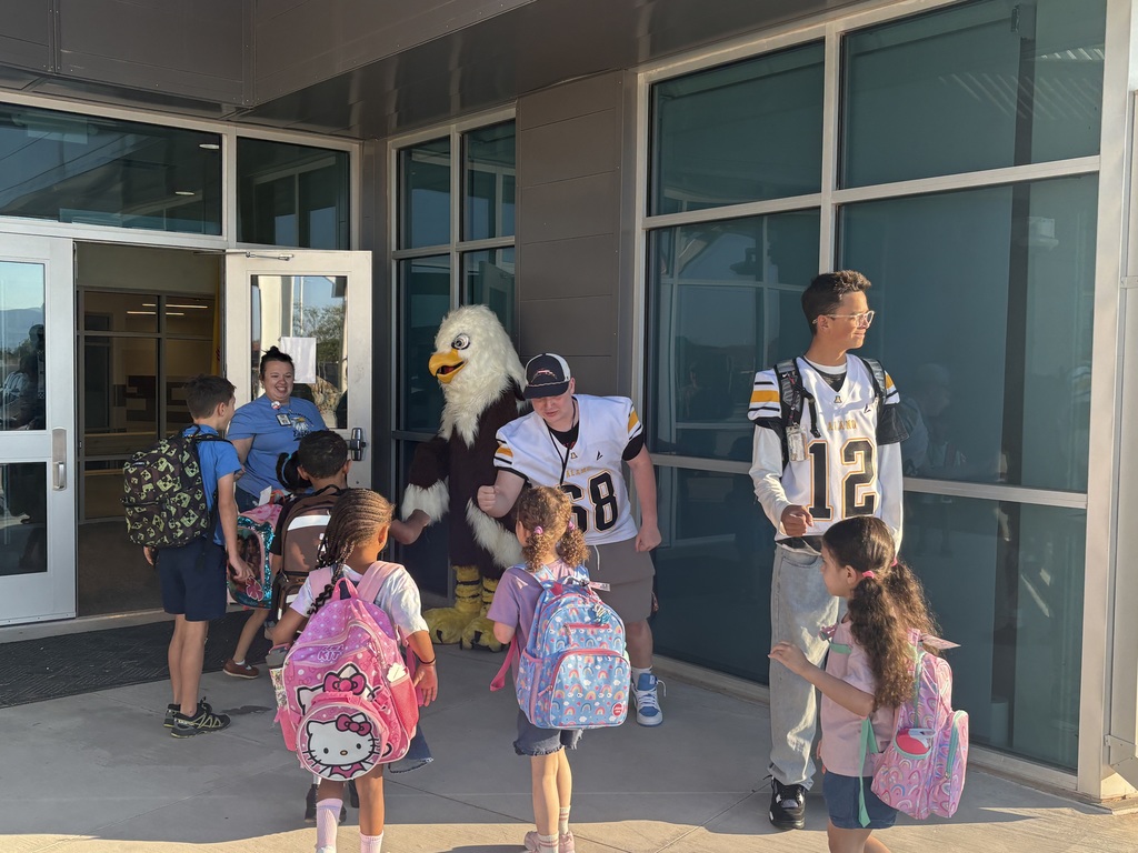 elementary school mascot and high school football players greeting elementary school students