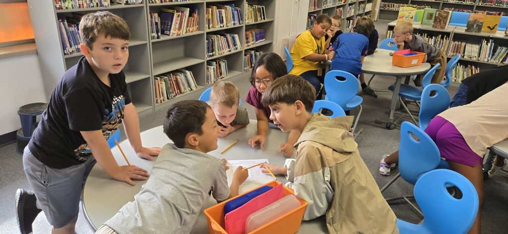 Students gathered around tables in a library working together