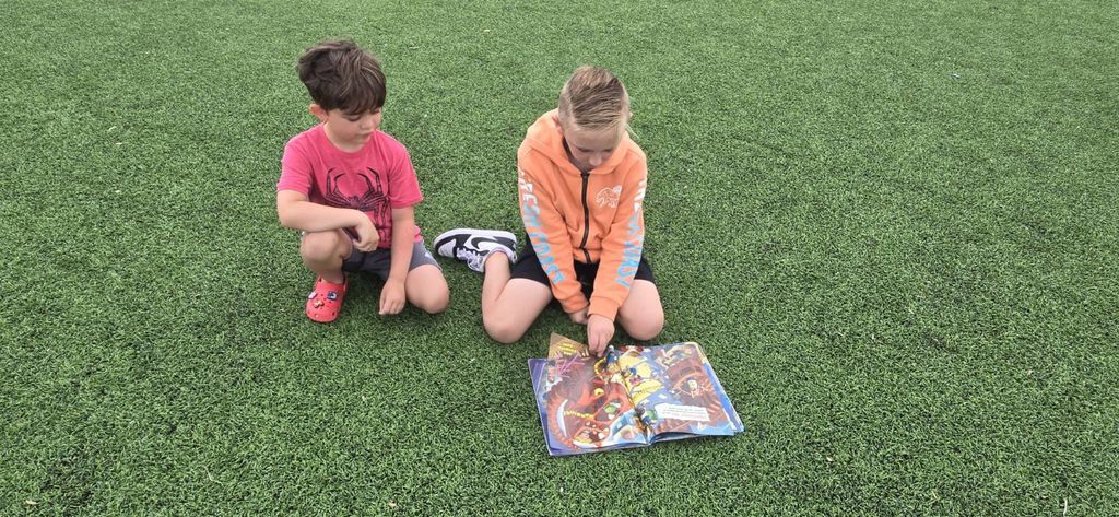 Two students sitting together on the turf looking through a book