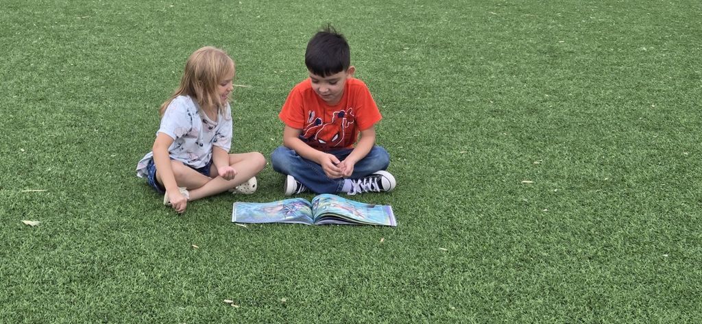 Two students sitting together on the turf looking through a book