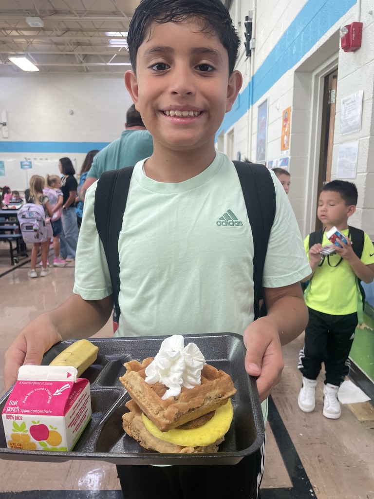 Student smiling with breakfast tray with juice, banana, and waffles