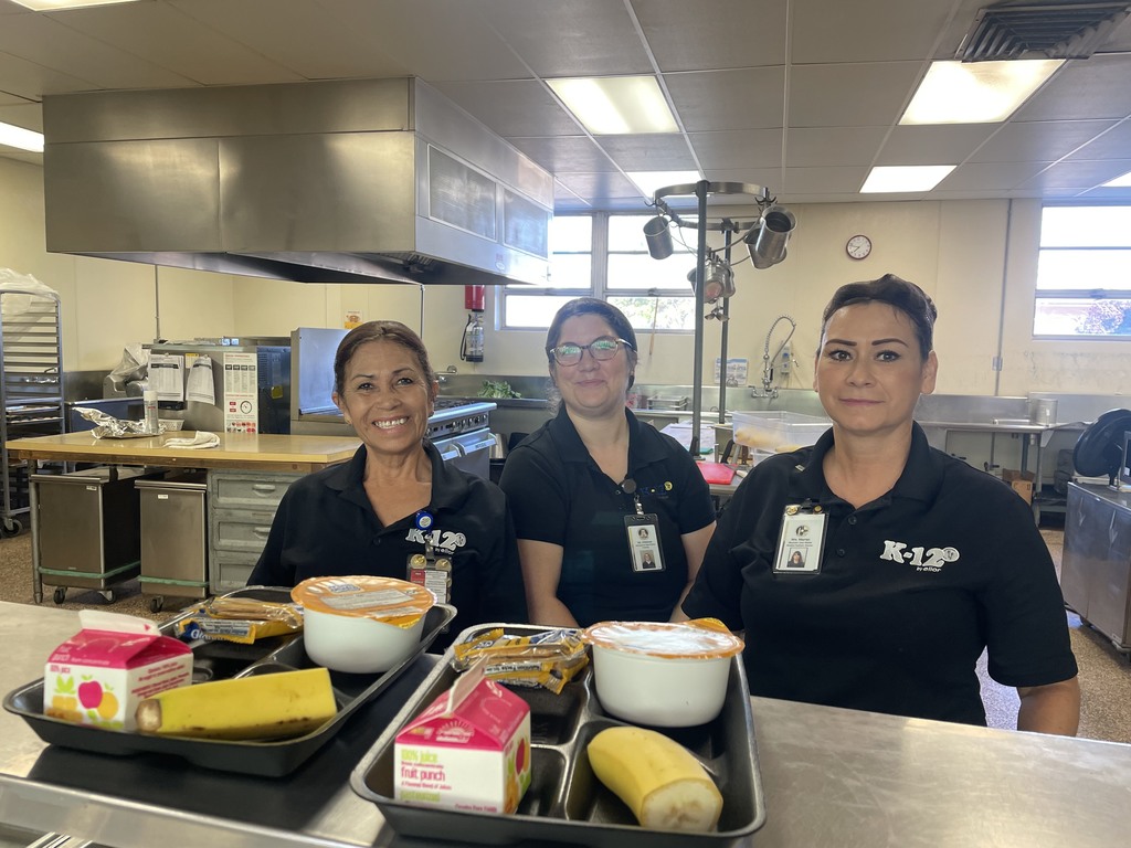 3 kitchen workers posing for a picture in the kitchen with breakfast trays in front of them
